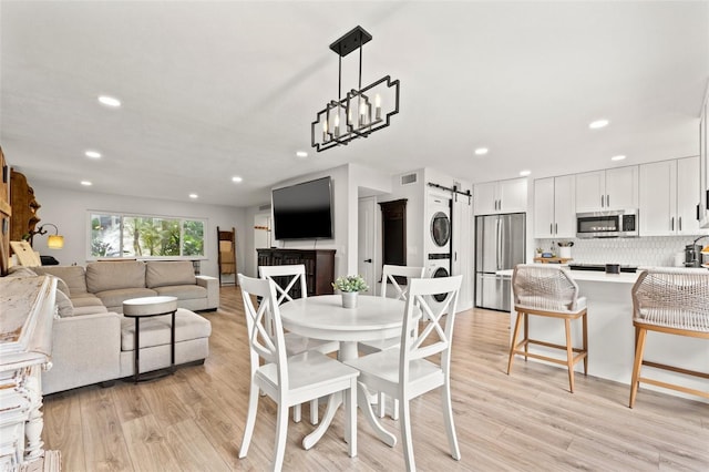 dining area featuring light wood finished floors, a barn door, stacked washer / dryer, and recessed lighting