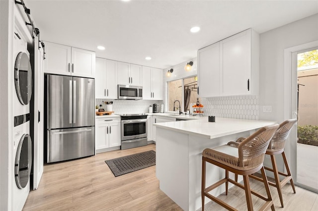 kitchen with a barn door, stacked washer / dryer, white cabinets, light countertops, and appliances with stainless steel finishes