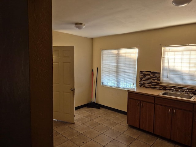 kitchen featuring light tile patterned floors, a sink, baseboards, light countertops, and backsplash