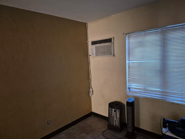 unfurnished room with an AC wall unit, dark tile patterned flooring, and baseboards