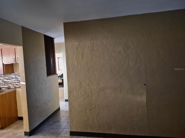 hall with light tile patterned floors and a textured wall