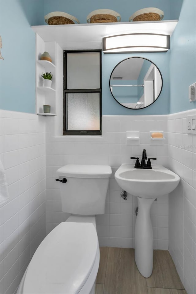 bathroom featuring a wainscoted wall, toilet, tile walls, and wood finished floors