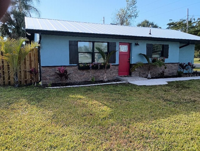 ranch-style house with metal roof, stone siding, a front yard, and stucco siding