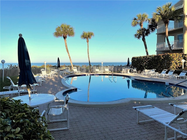 community pool featuring a patio area, a water view, and fence