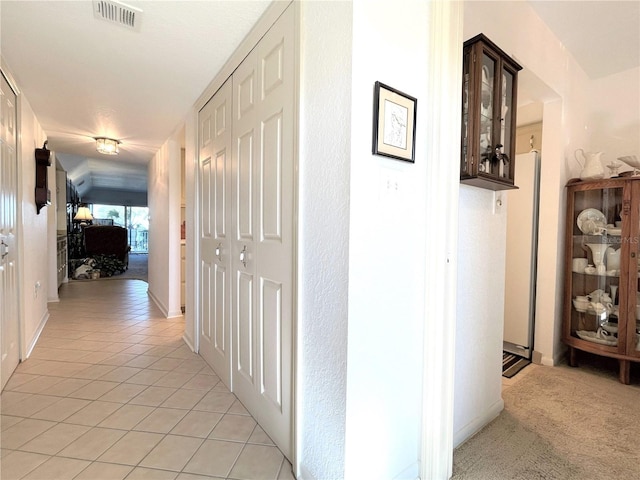 corridor with light tile patterned floors, visible vents, and light colored carpet