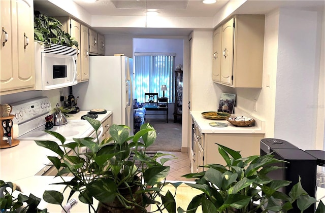 kitchen with white appliances, light colored carpet, cream cabinets, light countertops, and light tile patterned flooring