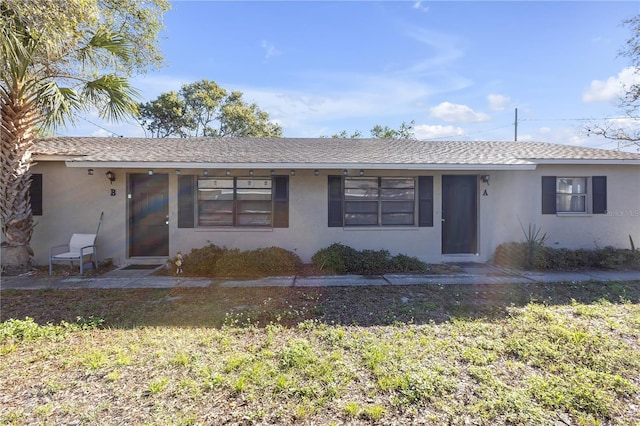 ranch-style house with a shingled roof, a front yard, and stucco siding