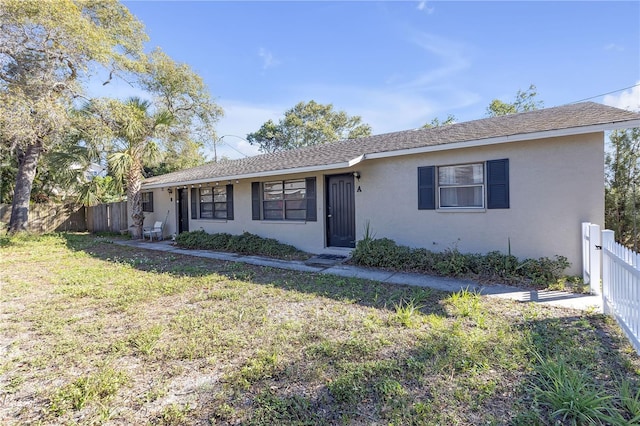 single story home with stucco siding, roof with shingles, fence, and a front yard