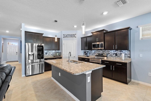 kitchen with a center island with sink, stainless steel appliances, visible vents, hanging light fixtures, and a sink