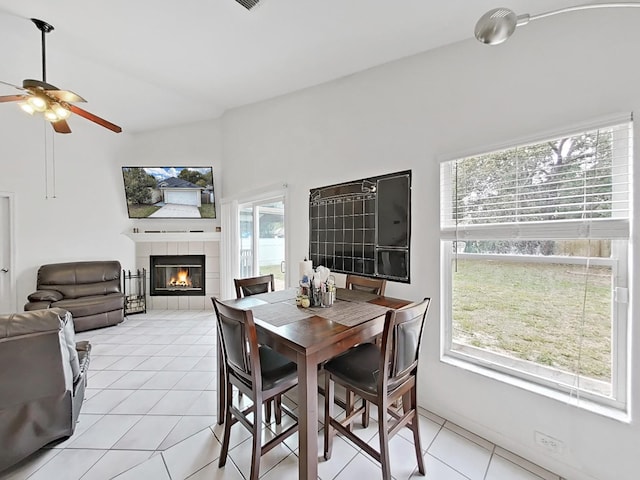 dining space featuring lofted ceiling, light tile patterned floors, a fireplace, and a ceiling fan