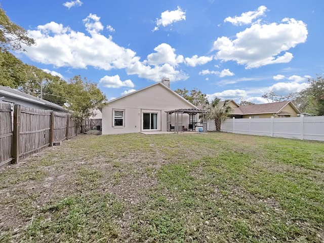 back of house with a yard, a chimney, stucco siding, a pergola, and a fenced backyard