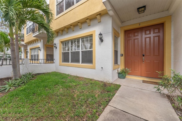 view of exterior entry featuring a yard and stucco siding