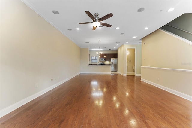 unfurnished living room with baseboards, ornamental molding, wood finished floors, and ceiling fan with notable chandelier