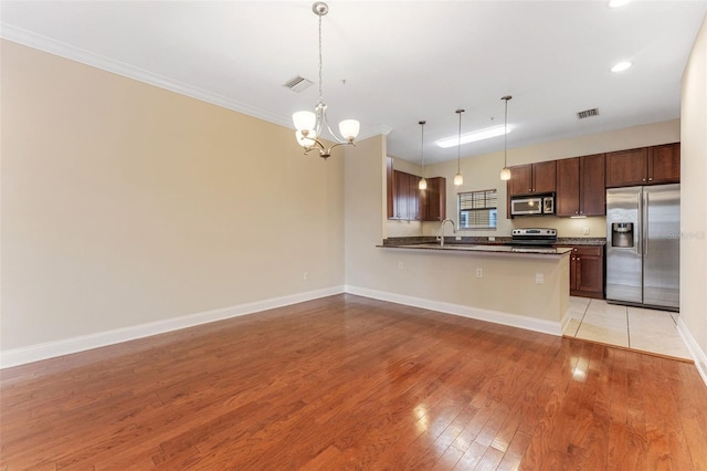 kitchen featuring light wood-style flooring, stainless steel appliances, open floor plan, hanging light fixtures, and dark countertops