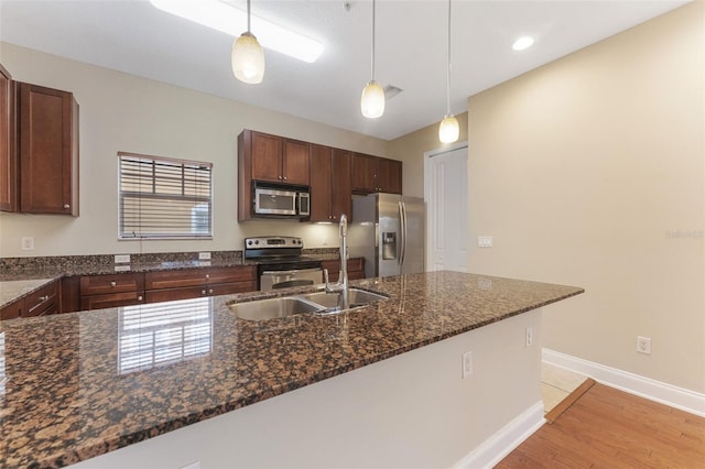 kitchen featuring stainless steel appliances, baseboards, light wood-type flooring, dark stone countertops, and decorative light fixtures