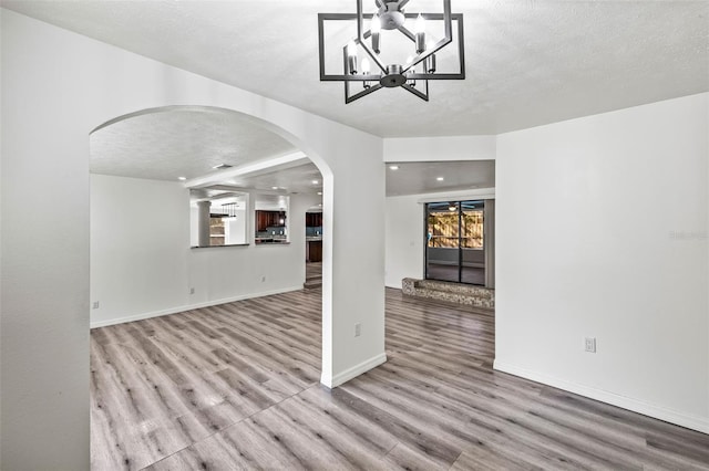 interior space featuring baseboards, light wood-style flooring, arched walkways, and a textured ceiling