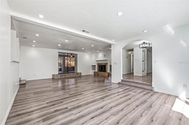 unfurnished living room featuring arched walkways, a fireplace with raised hearth, visible vents, and light wood-style floors