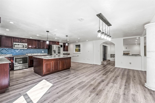 kitchen with stainless steel appliances, open floor plan, dark brown cabinets, a center island, and decorative light fixtures