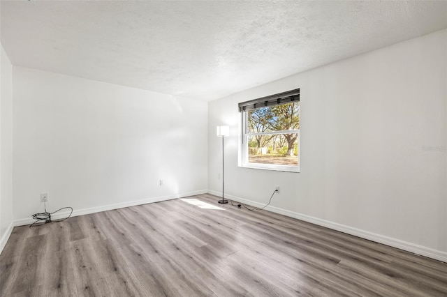 empty room with a textured ceiling, light wood finished floors, and baseboards