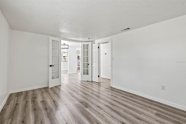 empty room with french doors, light wood finished floors, visible vents, a textured ceiling, and baseboards