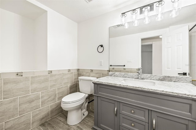 bathroom with wainscoting, toilet, wood finished floors, vanity, and tile walls