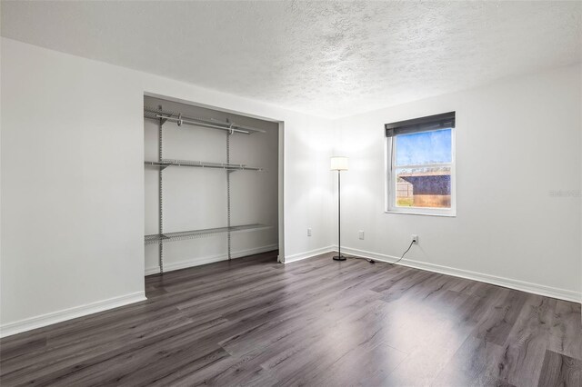 unfurnished bedroom featuring dark wood-style floors, a closet, a textured ceiling, and baseboards