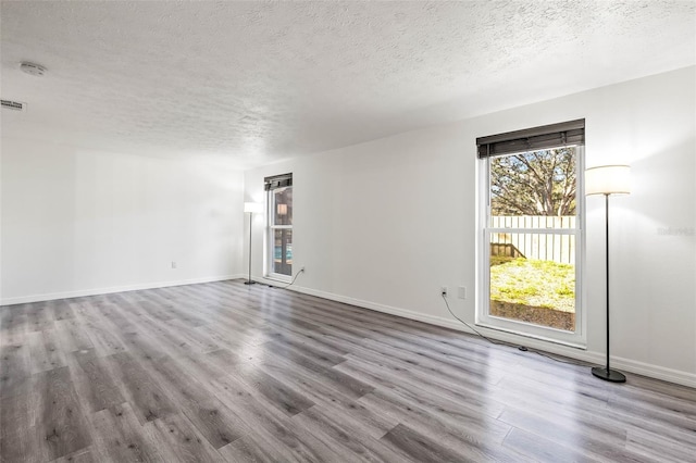 empty room with a textured ceiling, light wood-type flooring, visible vents, and baseboards