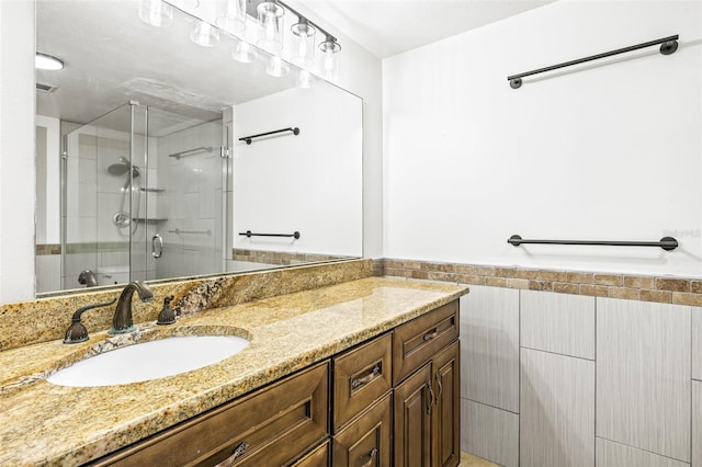 full bathroom featuring a stall shower, a wainscoted wall, tile walls, and vanity