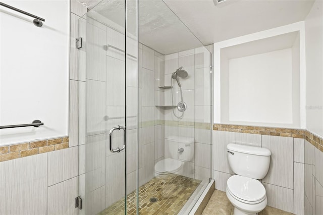 bathroom featuring toilet, a wainscoted wall, a shower stall, and tile walls