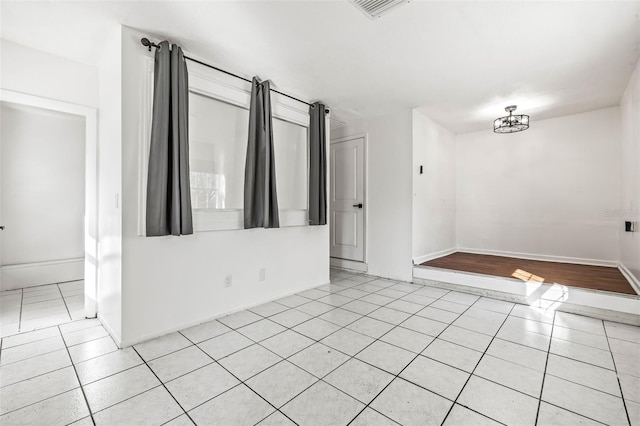 spare room with a notable chandelier, light tile patterned flooring, visible vents, and baseboards