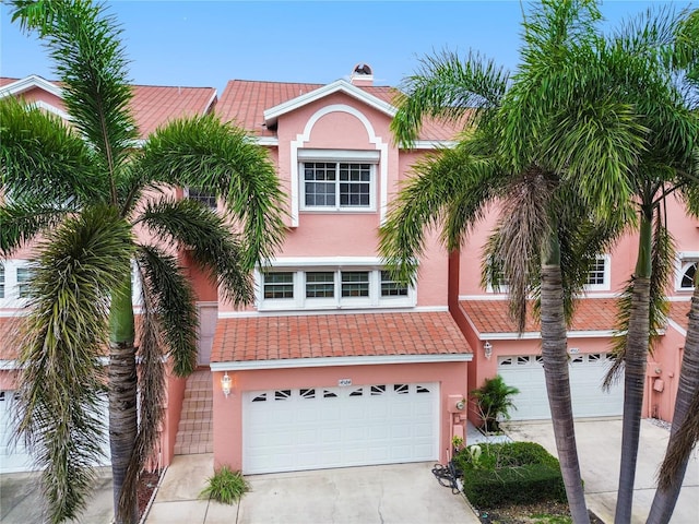 view of front facade featuring an attached garage, a chimney, stucco siding, concrete driveway, and a tiled roof