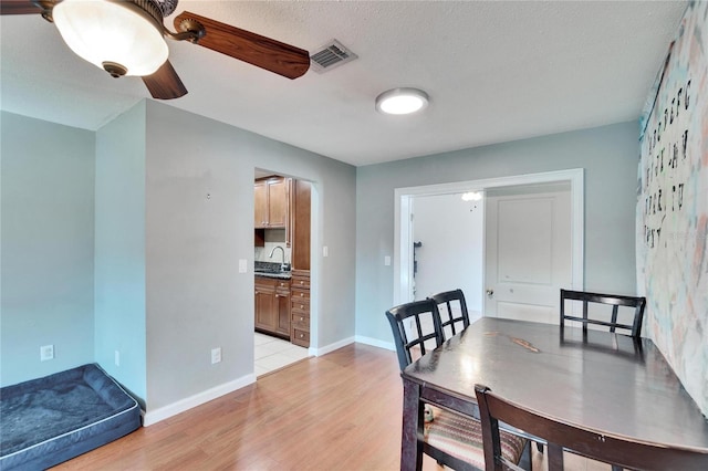 dining room with a textured ceiling, visible vents, baseboards, a ceiling fan, and light wood-type flooring