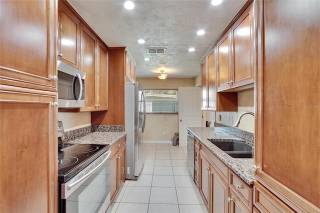 kitchen with brown cabinets, light stone countertops, stainless steel appliances, and a sink