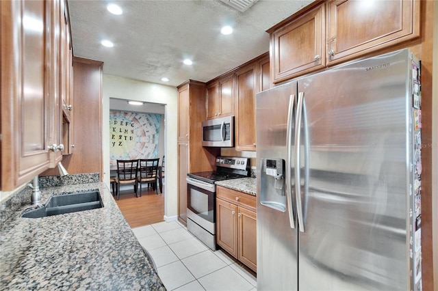 kitchen with brown cabinets, appliances with stainless steel finishes, a sink, and light stone countertops