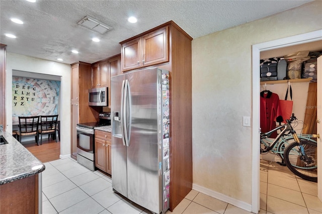 kitchen featuring appliances with stainless steel finishes, light tile patterned flooring, visible vents, and brown cabinets