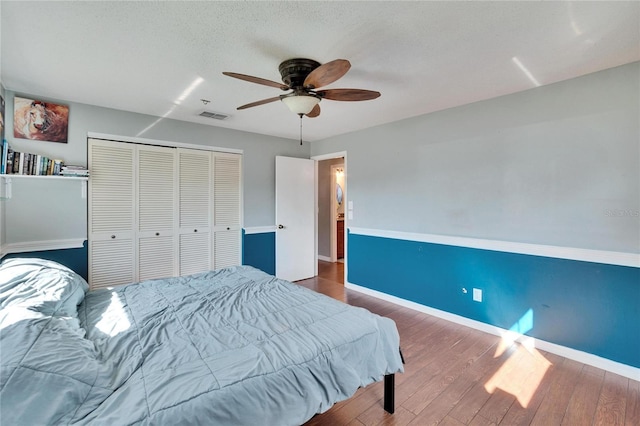 bedroom with wood finished floors, a ceiling fan, visible vents, baseboards, and a closet