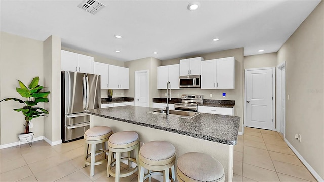 kitchen with stainless steel appliances, a sink, visible vents, dark countertops, and a center island with sink