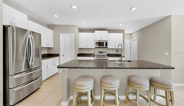 kitchen featuring a breakfast bar area, stainless steel appliances, a kitchen island with sink, a sink, and white cabinetry