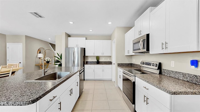 kitchen with stainless steel appliances, dark countertops, a kitchen island with sink, and white cabinetry