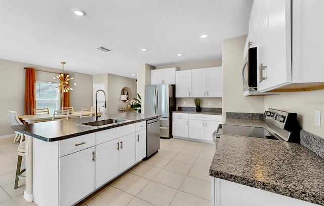 kitchen with stainless steel appliances, dark countertops, white cabinetry, and an island with sink