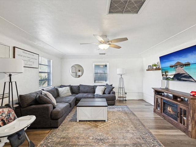 living area with a ceiling fan, baseboards, visible vents, and wood finished floors