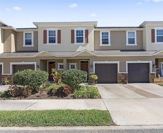 view of property with a garage, stone siding, driveway, and stucco siding