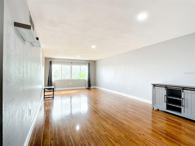 unfurnished living room with recessed lighting, wood finished floors, and baseboards