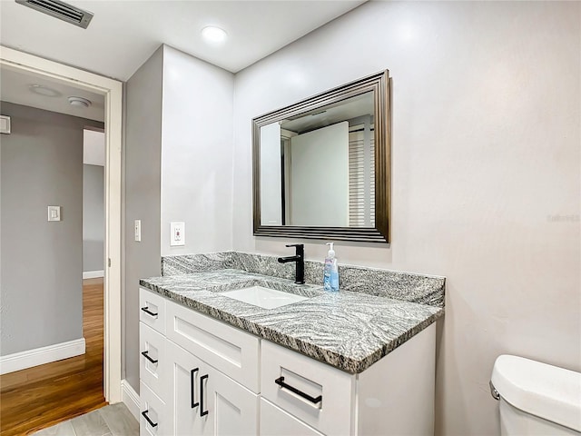 bathroom featuring visible vents, toilet, vanity, wood finished floors, and baseboards