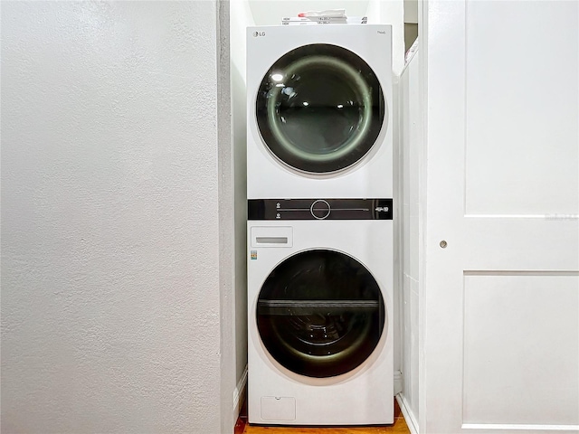 clothes washing area featuring a textured wall, laundry area, and stacked washer / dryer