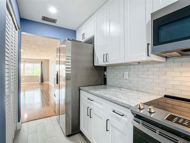 kitchen with visible vents, white cabinets, light stone countertops, wood tiled floor, and stainless steel appliances