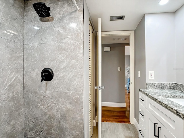 bathroom featuring visible vents, vanity, wood finished floors, tiled shower, and baseboards