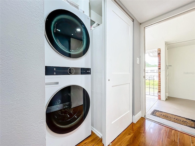 washroom featuring laundry area, a textured wall, stacked washer / drying machine, and wood finished floors