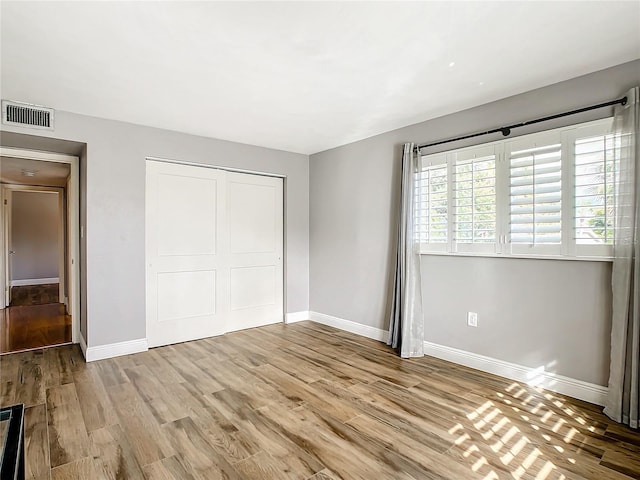 unfurnished bedroom featuring light wood-type flooring, baseboards, visible vents, and a closet