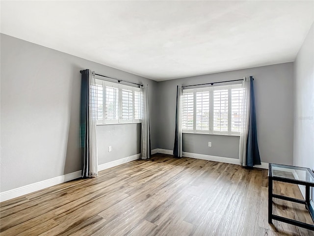 empty room featuring a wealth of natural light, light wood-style flooring, and baseboards